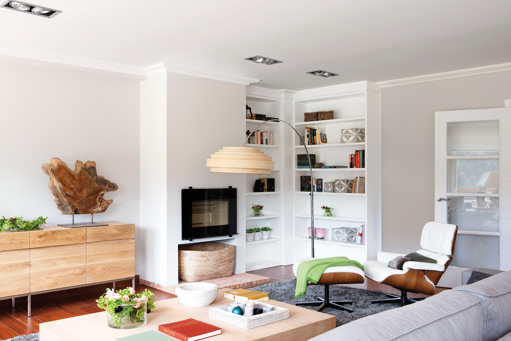 Salón con sofá gris, butaca blanca de madera, aparador de madera y chimenea.