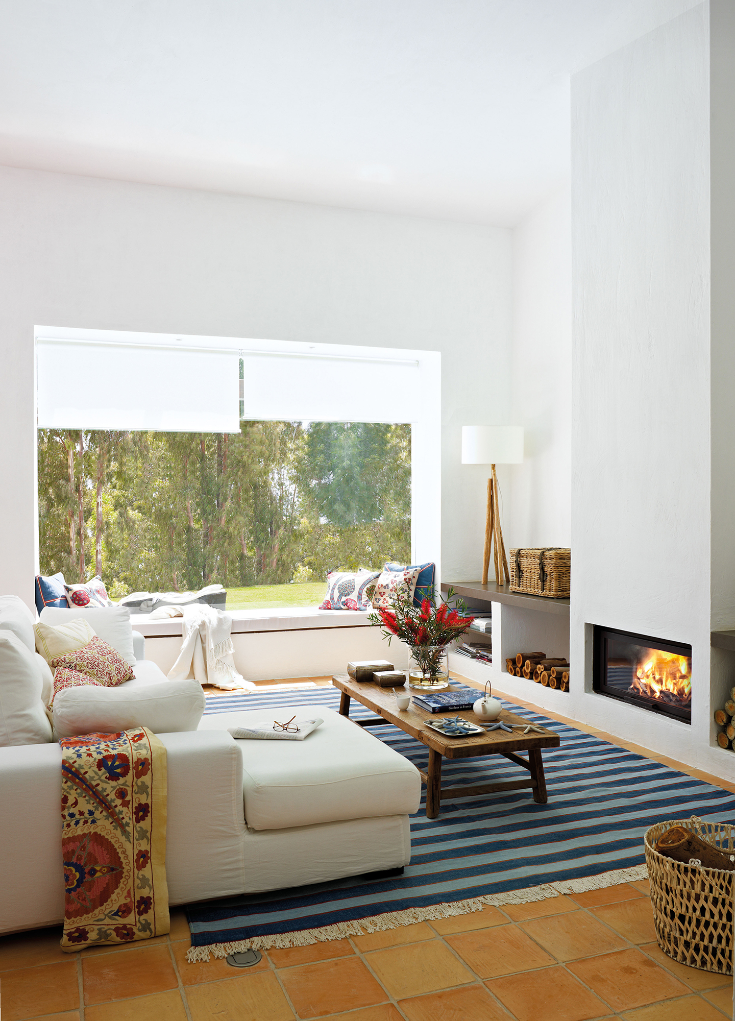 Salón moderno con look mediterráneo con alfombra de rayas, sofá blanco con chaise longue y chimenea.