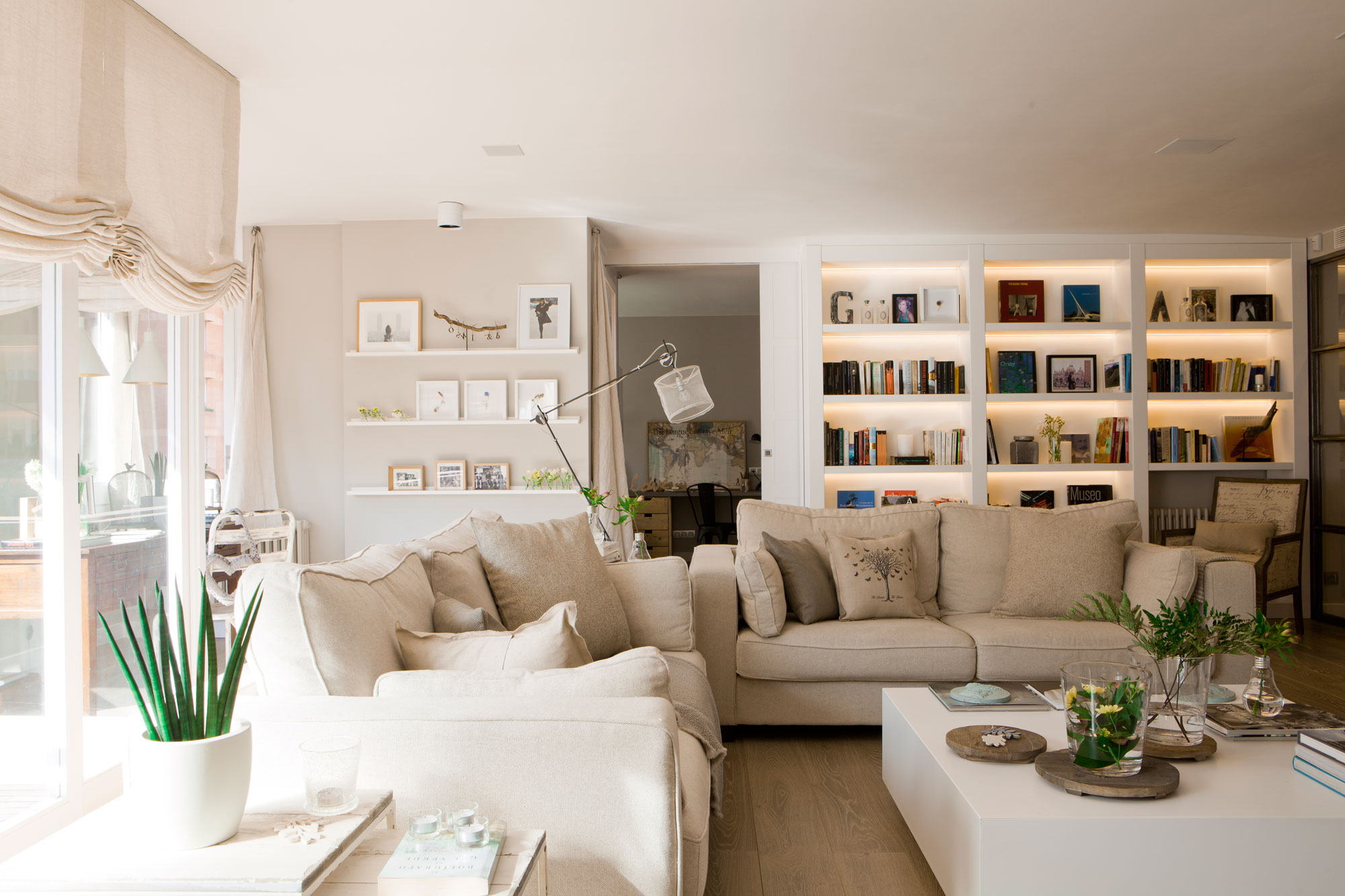 Salón moderno en blanco con librerías, sofás grises, mesa de centro blanca. 