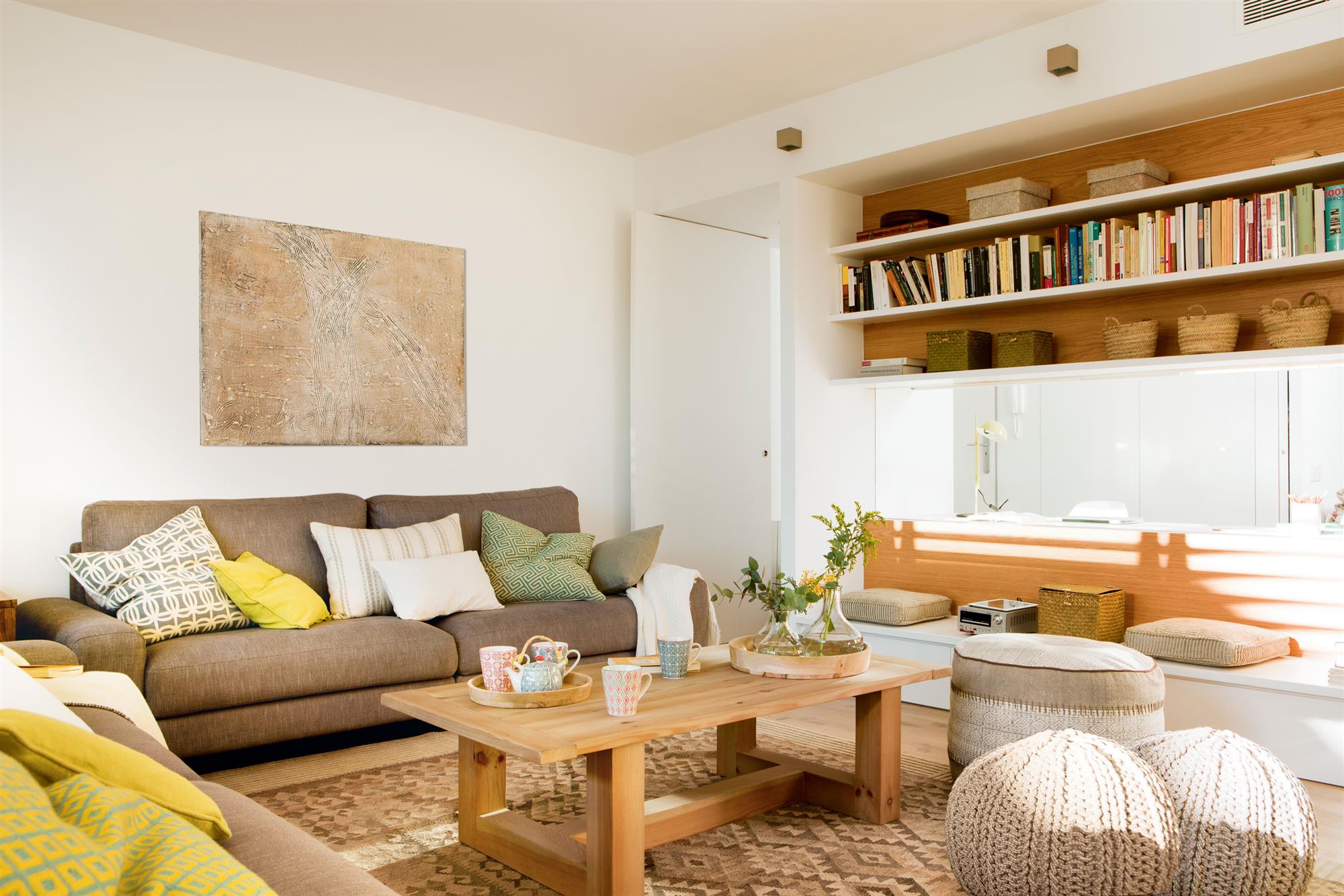 Salón moderno con librería a lo alto, puffs, mesa de madera y sofá gris oscuro. 