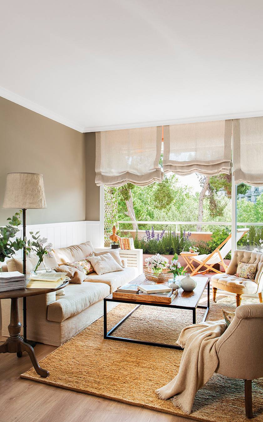 Salón con arrimadero blanco y paredes, sofá y butacas de color beige. 