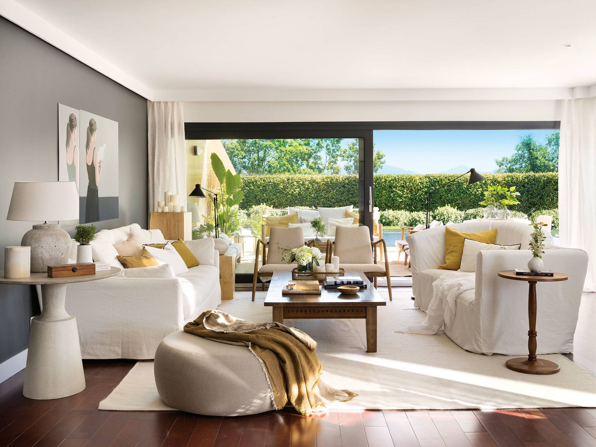 Un salón con sofás blancos y pared gris con grandes ventanales al exterior.