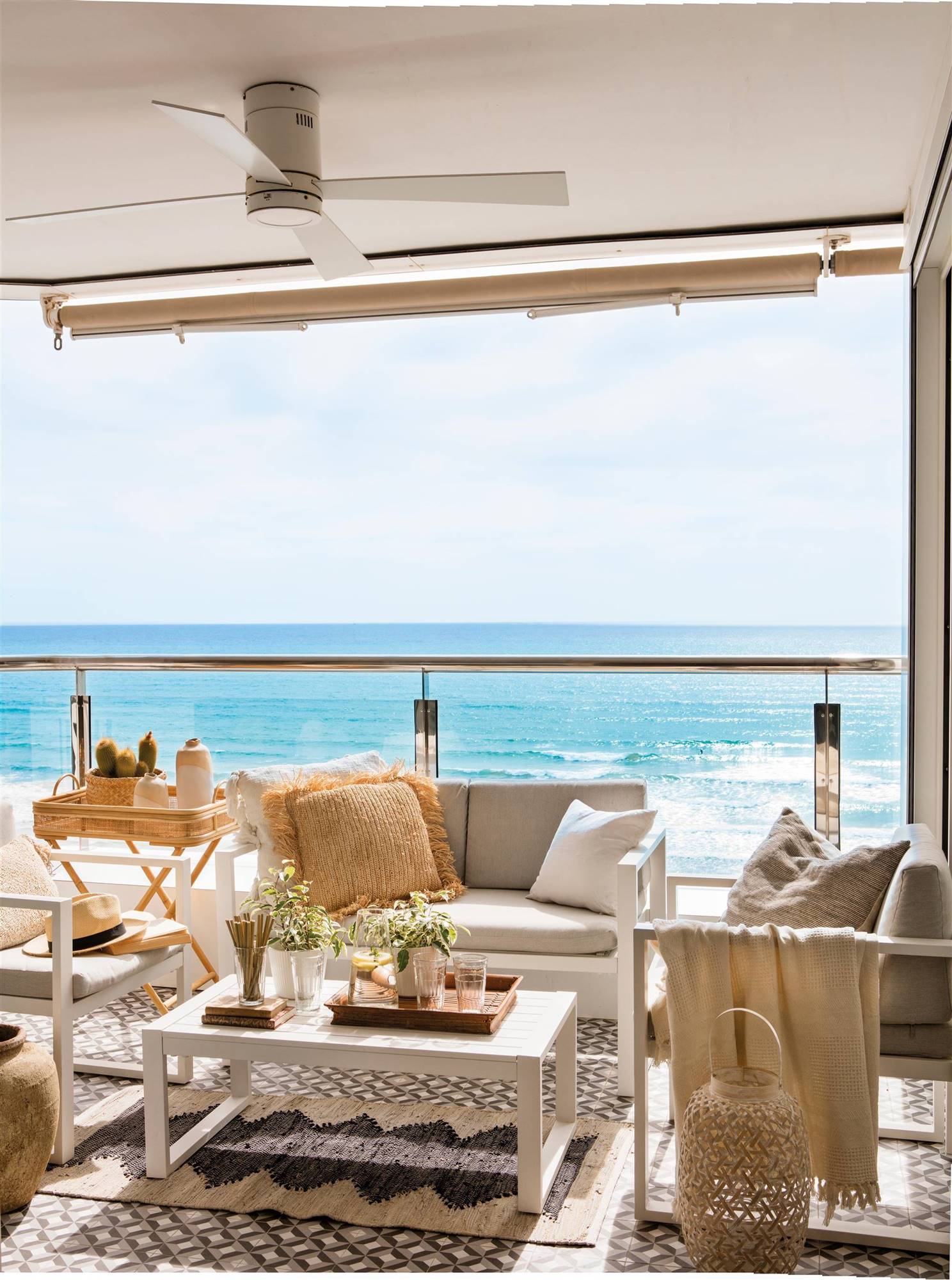 Terraza con muebles blancos y barandilla de cristal. 