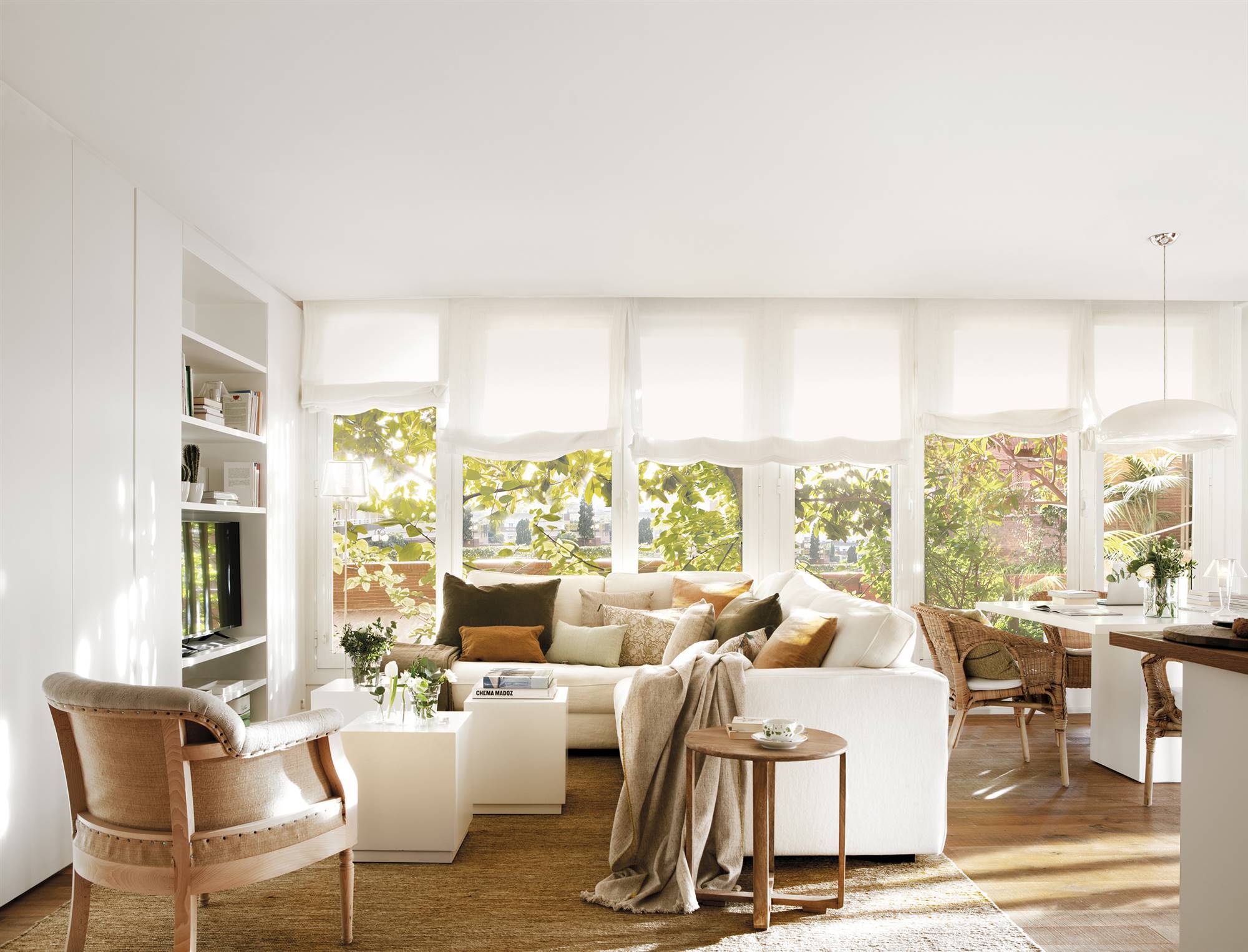 Salón blanco con sofá rinconero y grandes ventanales.