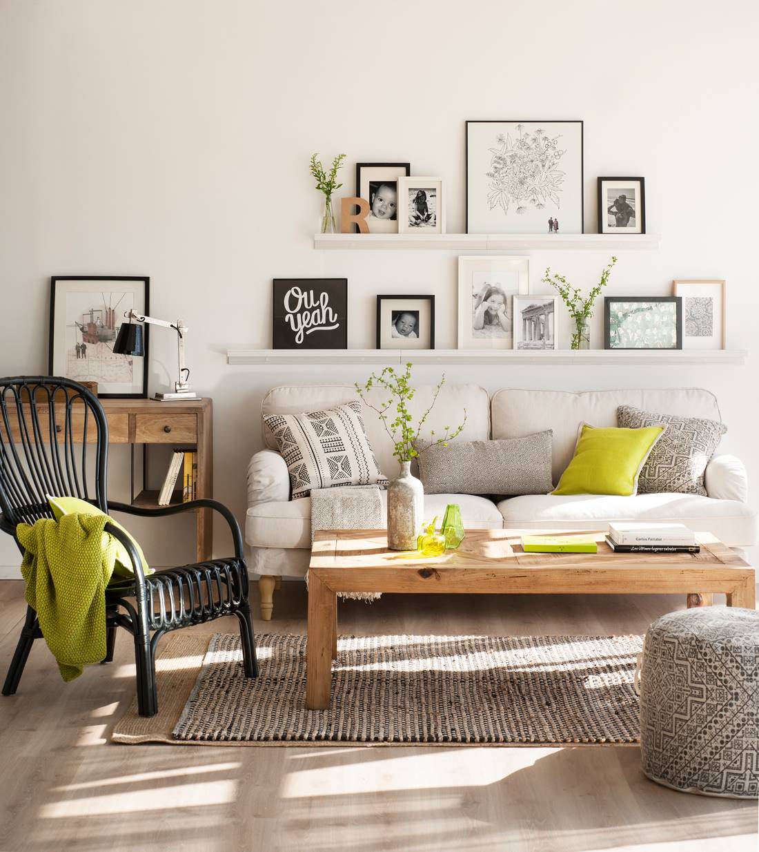 Salón pequeño con sofá gris, butaca de mimbre negra y estantes en la pared. 