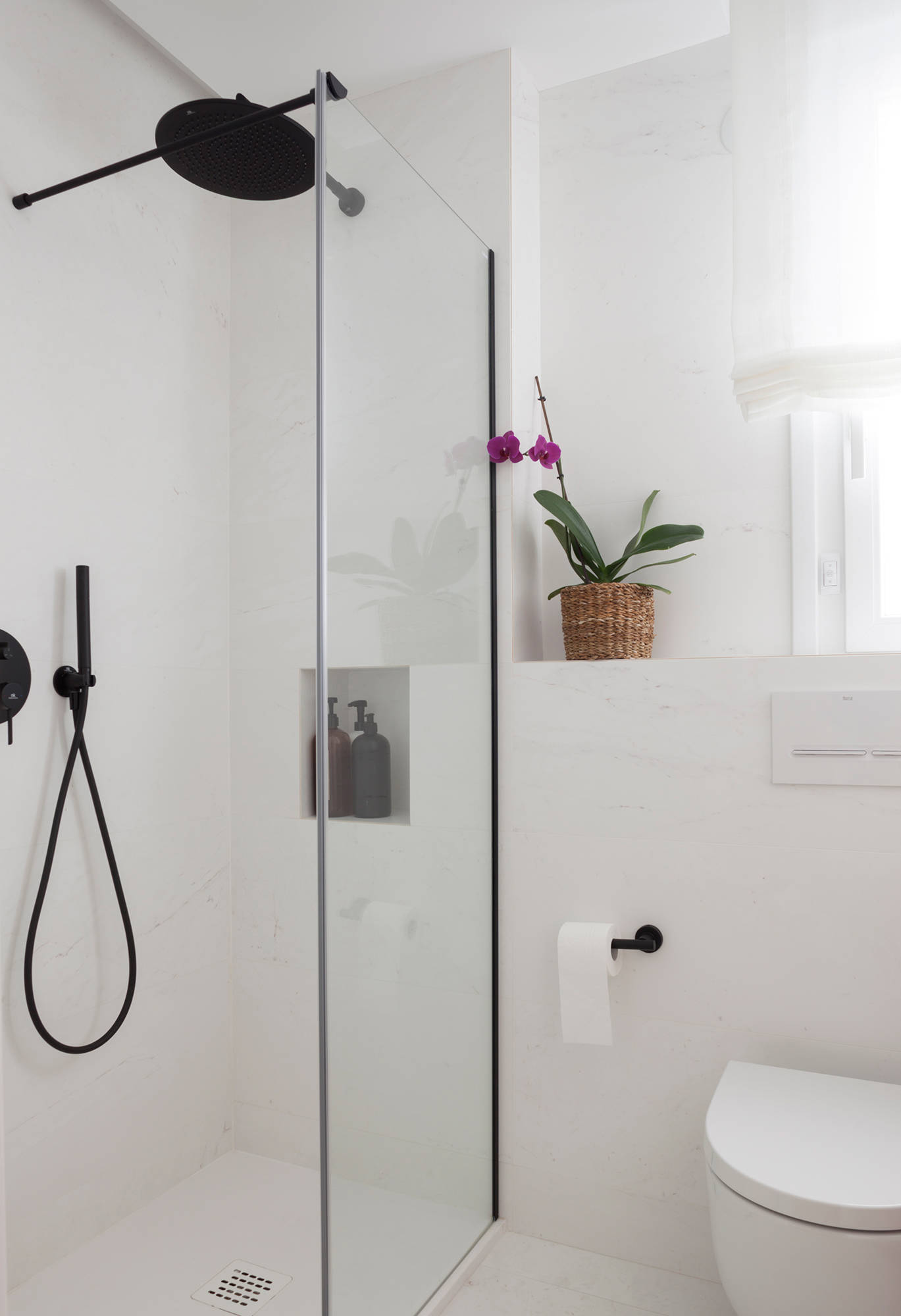 Baño con revestimiento de mármol y estantería de obra sobre el inodoro.