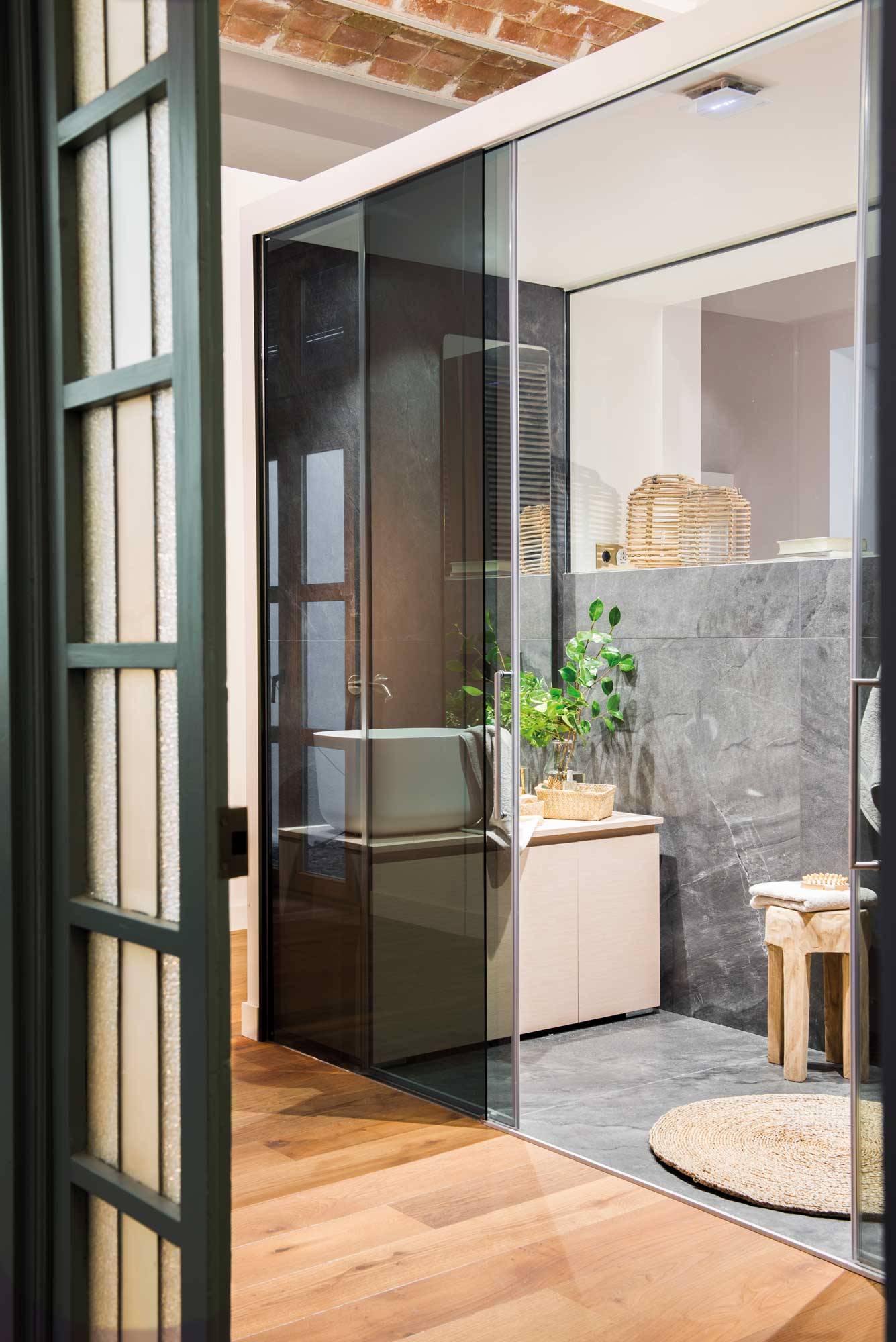 Baño con puertas correderas de cristal y revestimiento con acabado en mármol negro. 