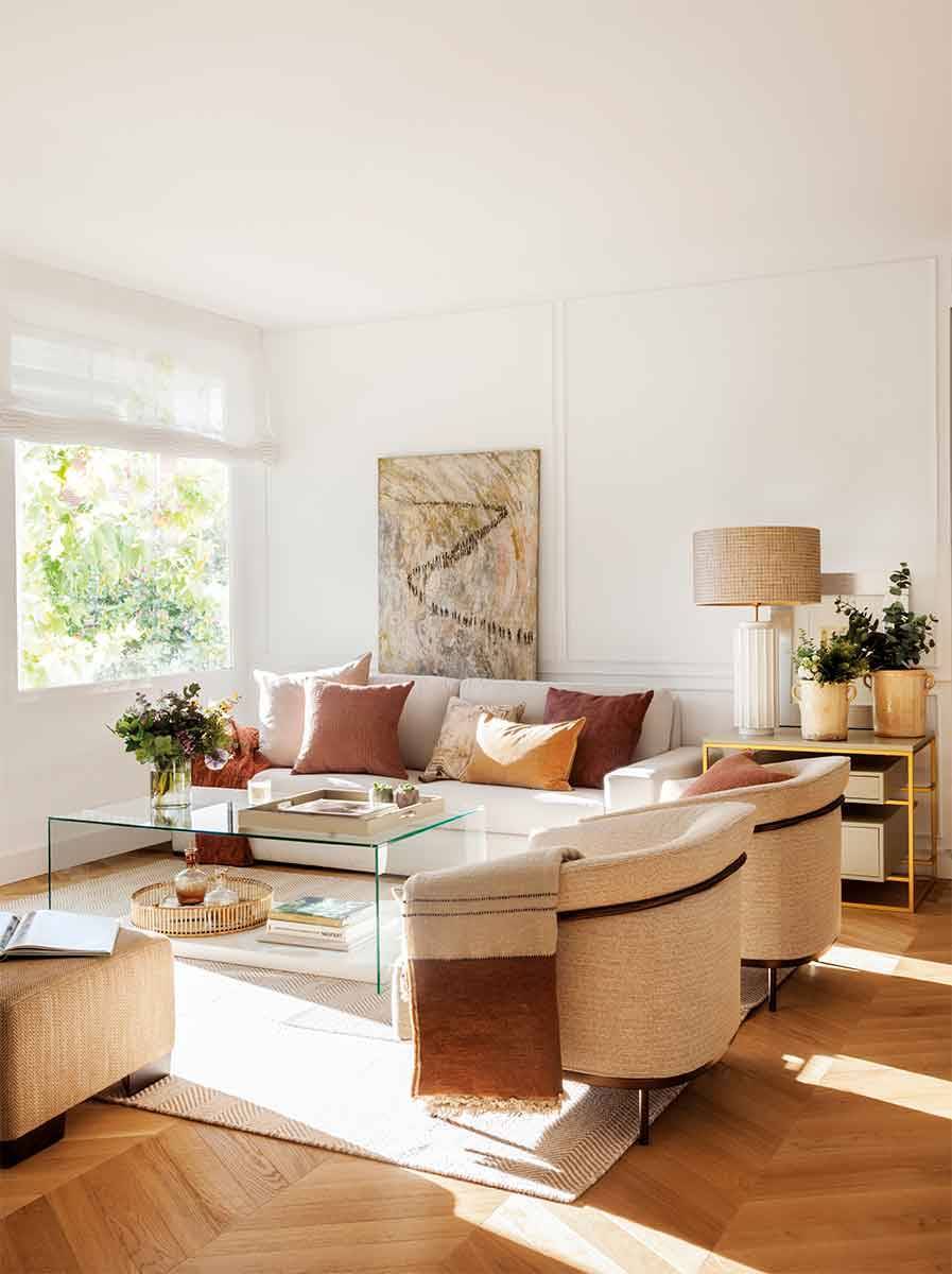 Salón pequeño con sofá beige, butacas modernas y mesa de centro de cristal. 