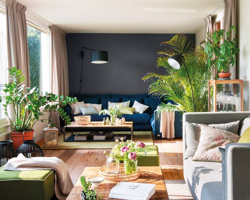 Salón moderno con pared y sofá azul, y alfombra y puffs verdes.
