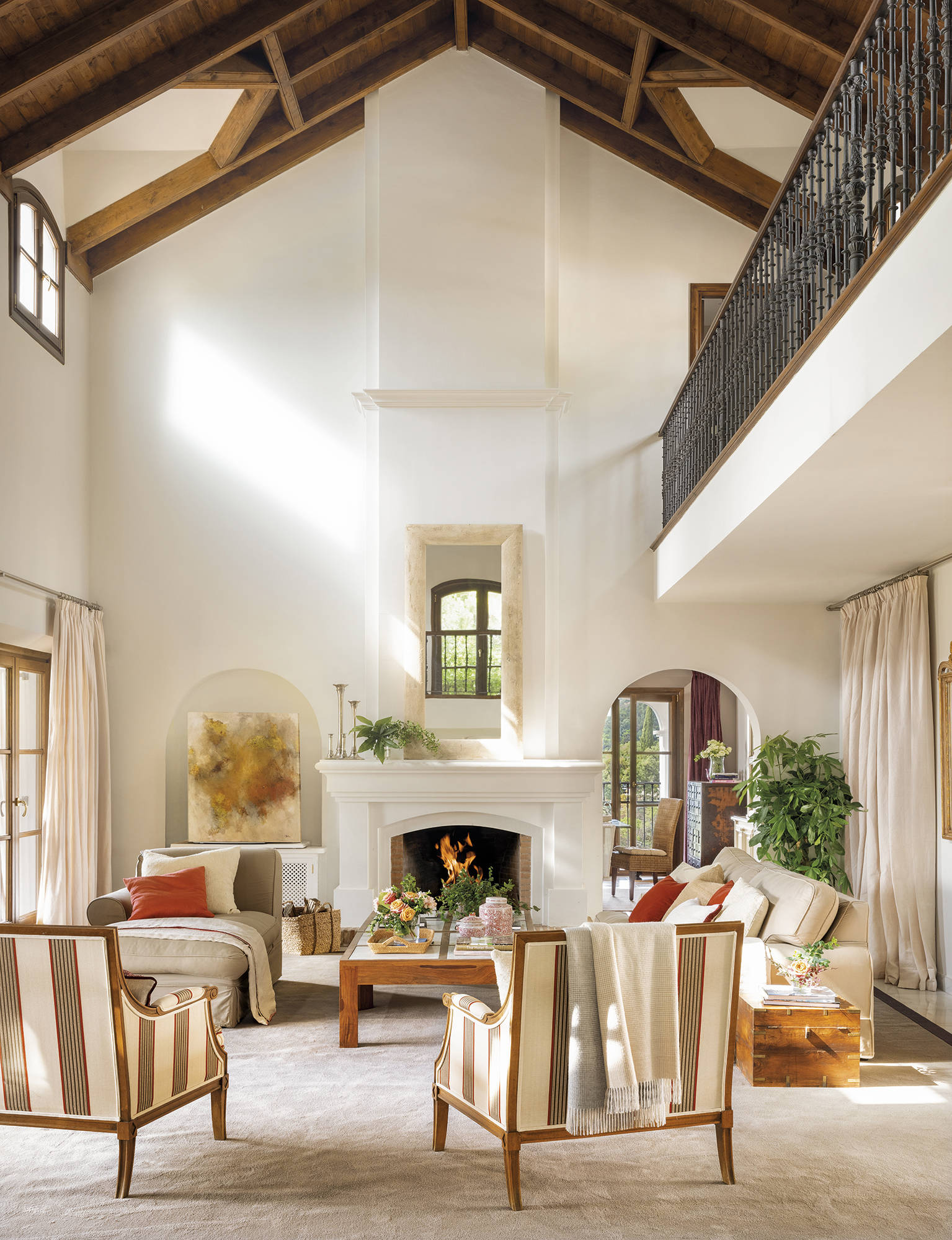 Salón blanco con techo a doble altura, chimenea, moqueta y butacas a rayas.