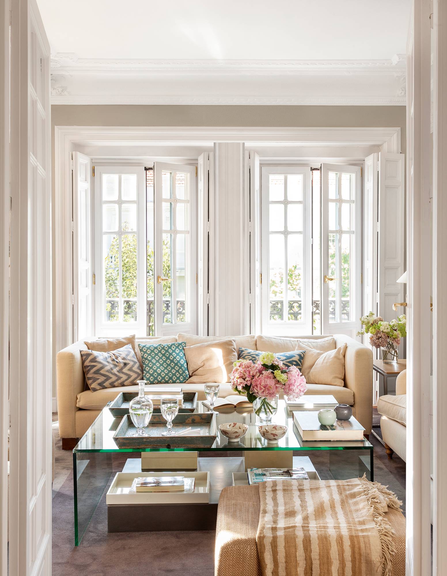 Salón clásico con grandes ventanales y mesa de centro de cristal. 