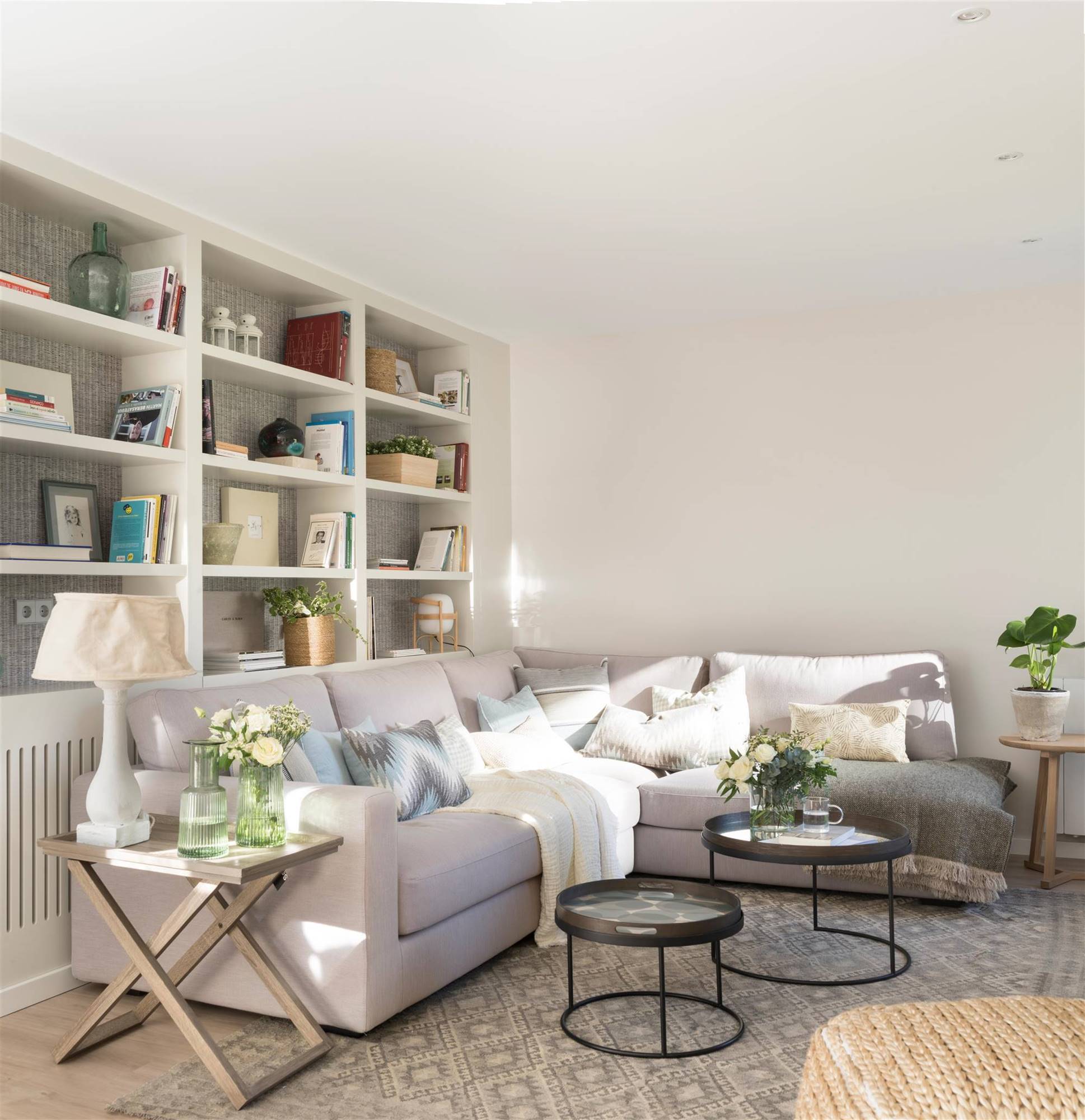 Salón con sofá rinconero de color gris y pared blanca. 