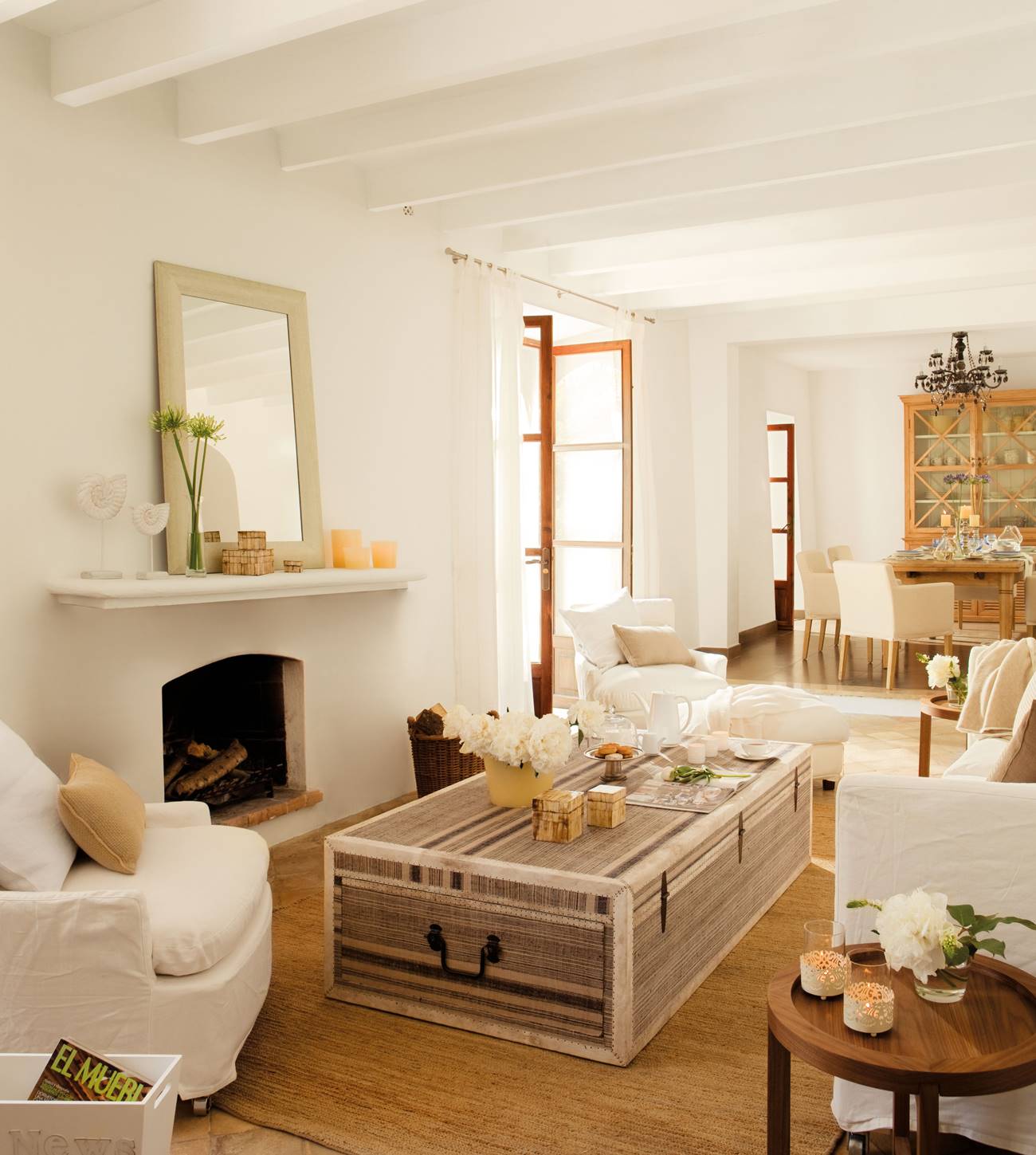Salón pequeño blanco con chimenea y baúl como mesa de centro. 