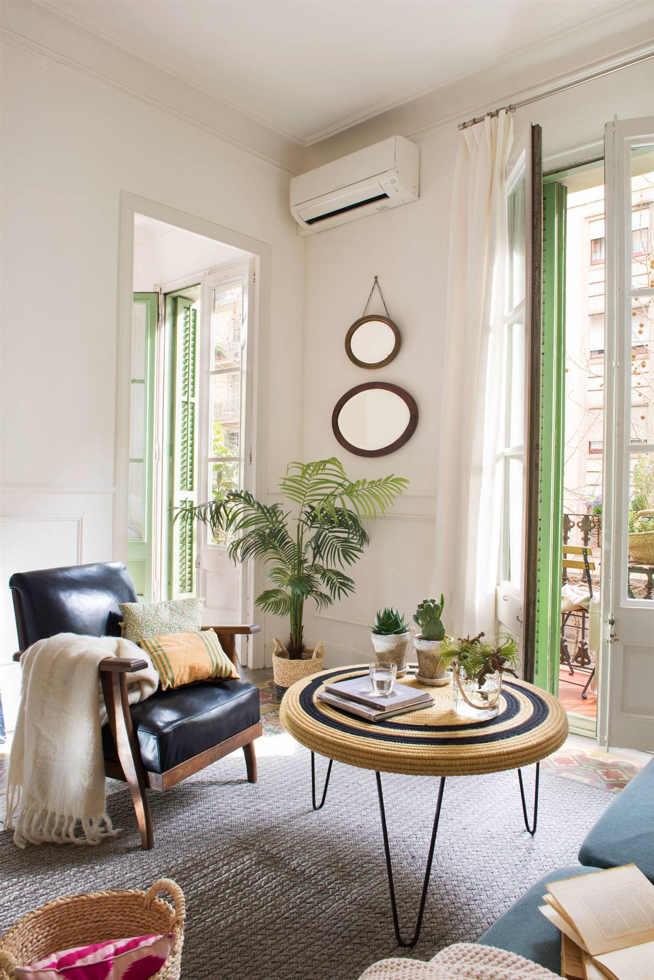 Salón boho con mesa de centro redonda de fibras, butaca negra y ventana verde.