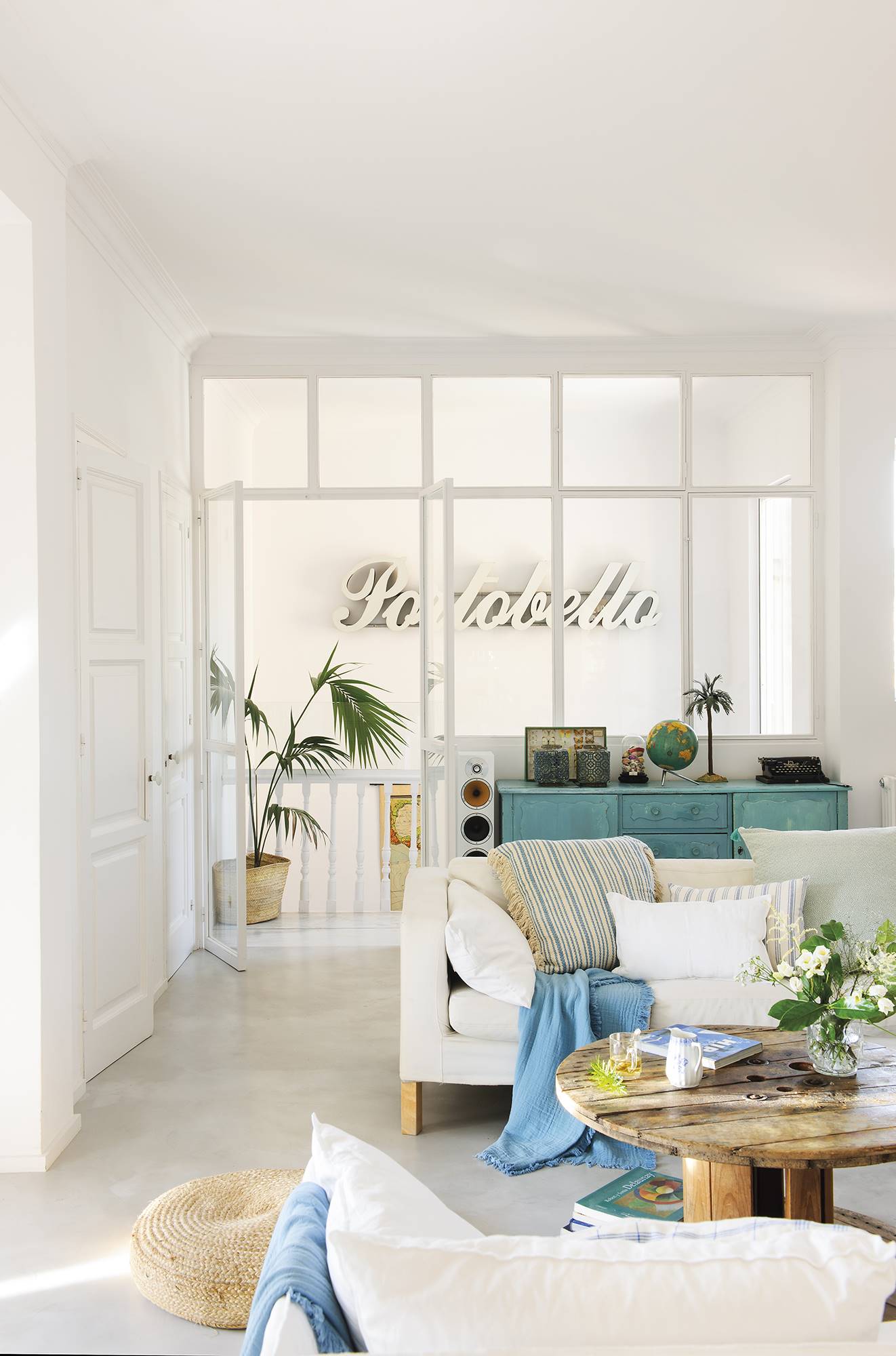 Salón blanco y moderno con mesa de centro de madera y puff de fibras.